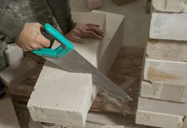 a-man-saws-a-block-of-foam-concrete-with-a-close-u-2023-11-27-05-13-03-utc.jpg